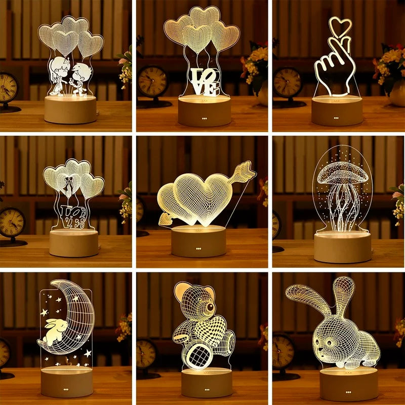 Romantic 3D LED lamps for home decor and party lighting. Variety of designs including hearts, cloud, couple silhouettes, and animal shapes. Placed on a wooden surface with decorative flowers in the background.