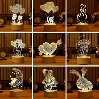 Romantic 3D LED lamps for home decor and party lighting. Variety of designs including hearts, cloud, couple silhouettes, and animal shapes. Placed on a wooden surface with decorative flowers in the background.