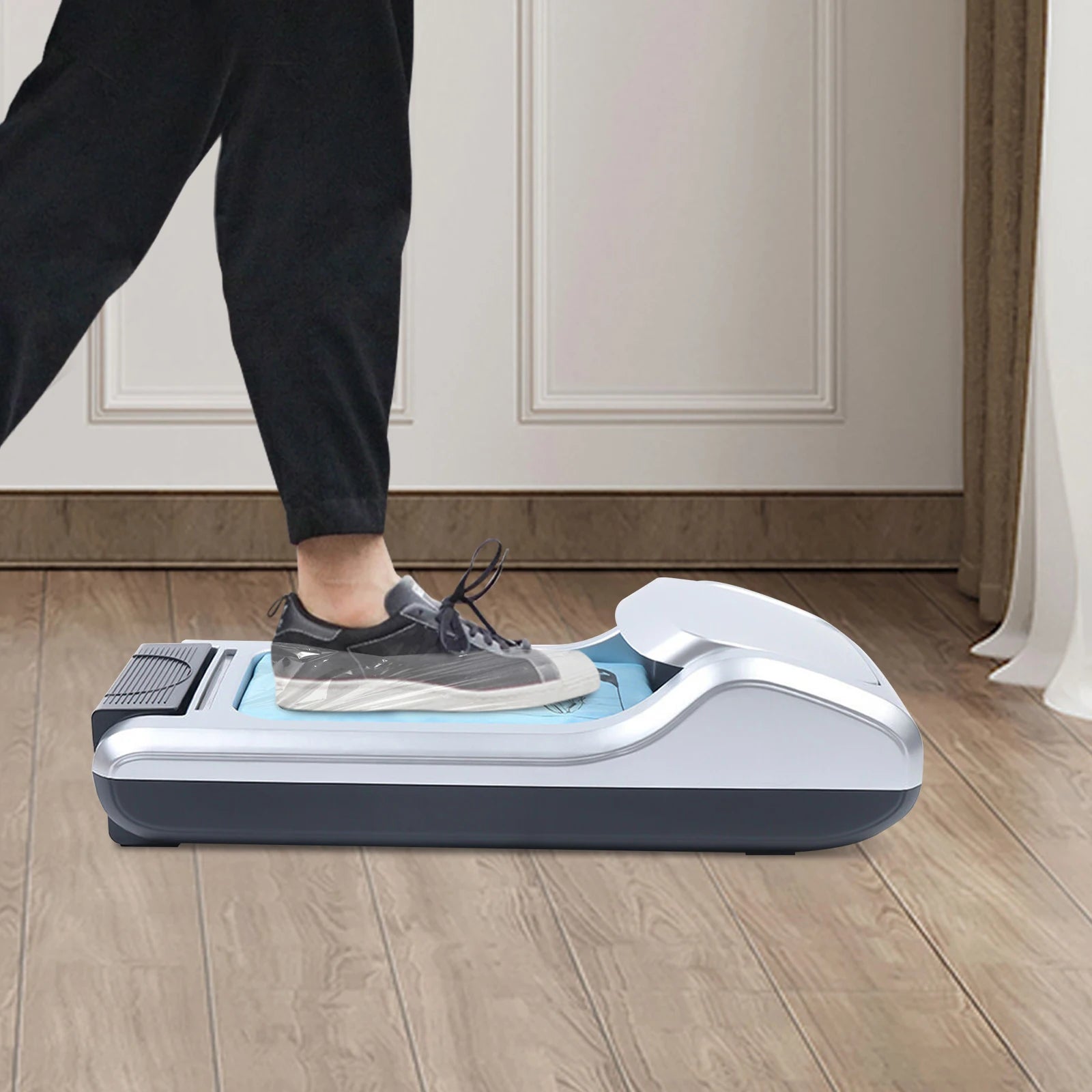 Automatic shoe cover dispenser machine with hands-free operation. The machine is shown on a wooden floor, with a person's legs and shoes visible nearby. The product appears to be a smart device designed to efficiently dispense shoe covers, providing a convenient solution for maintaining cleanliness.